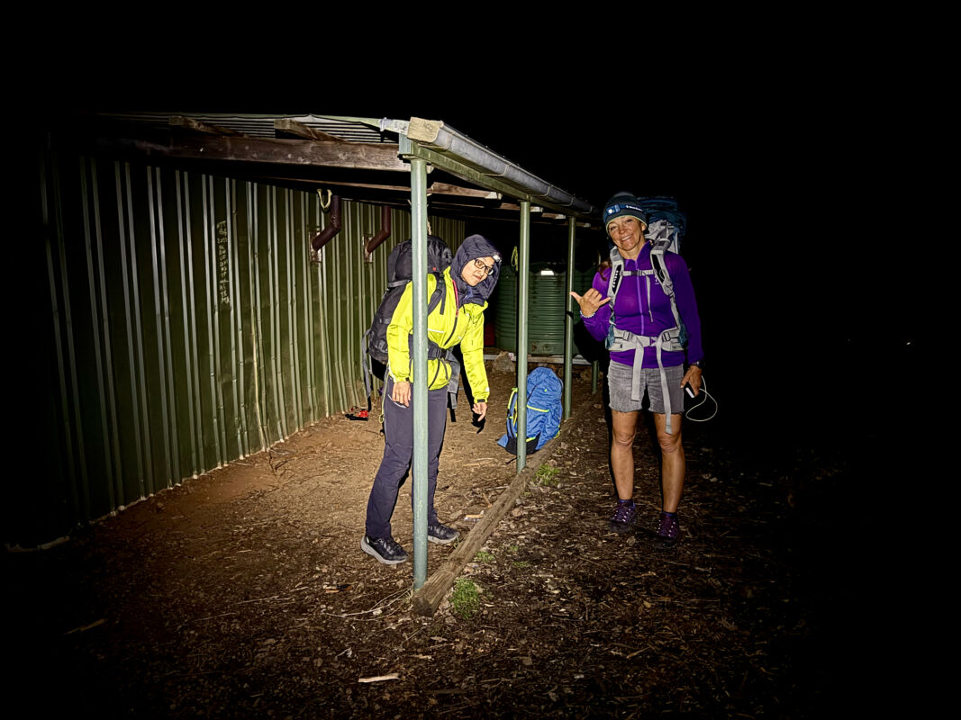 Climbers are shown in the cone of a head torch. Around them it is dark. They are beside Balor Hut and look happy. They are leaving for their adventure climb.